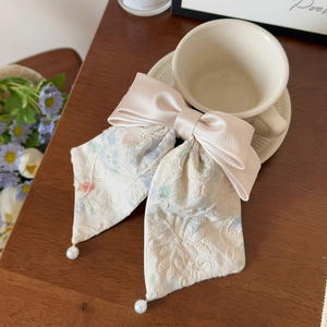 Detail of embroidered lace bow hair clip with pearls next to a coffee cup on wood