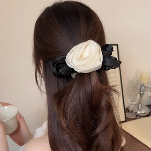 Detailed view of 3D mesh rose hair clip with black satin bow on model's wavy brown hair