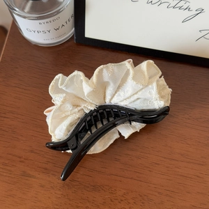 Close-up of elegant lace and pearl bow hair claw clip on a warm wooden surface