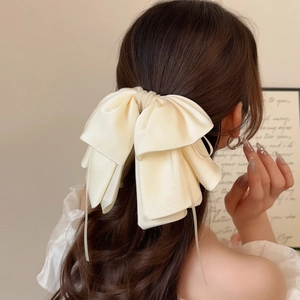 Elegant cream satin bow hair clip with pearls and long ribbons shown on hair