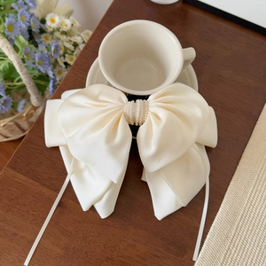Detail of cream satin bow hair clip with faux pearl center and long ribbon streamers