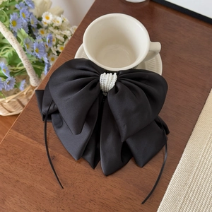 Detail of elegant black satin bow hair clip with luxury white pearl rows and long ribbons