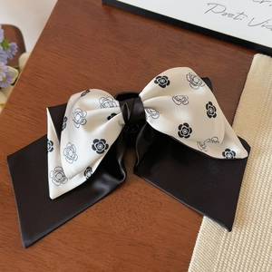 Elegant camellia bow hair claw clip in black and white silk fabric on a wooden desk