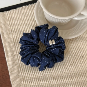 Détail d'un chouchou bleu marine à pois sur un tapis beige avec une tasse à café