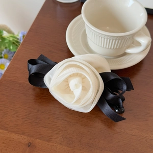 Macro detail of 3D mesh rose hair clip with elegant black satin ribbons on wood