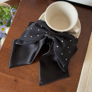 Close-up of a large black satin polka dot bow hair clip with ribbons on a wooden desk
