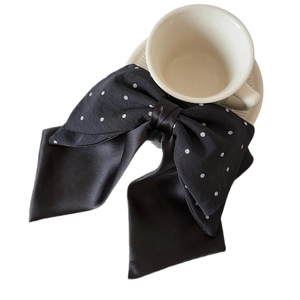 Elegant black polka dot bow hair clip with satin finish and long streamers on a ceramic cup