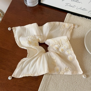 Close-up of beige hair scrunchie with yellow floral embroidery and pearl pendant