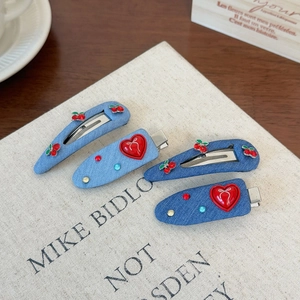 Detail of four denim hair clips featuring cherry rhinestones and red heart accents