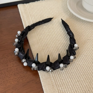 Détail d'un serre-tête en satin noir avec pointes, perles et cristaux sur un tapis tressé