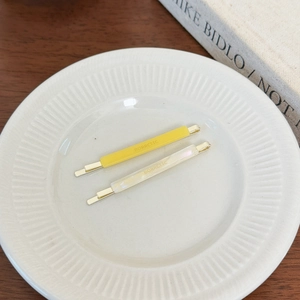 Detail of yellow and white acetate hair clips on a ceramic plate in a minimalist setting