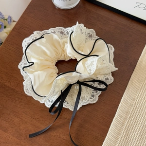 Détail d'un chouchou en satin crème avec dentelle et long nœud en velours noir à perle