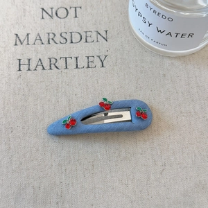 Close-up of denim blue hair clip with cute cherry rhinestones on a beige fabric background