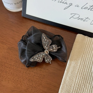 Détail d'une pince à cheveux avec nœud en maille noire et ornement papillon en strass étincelants