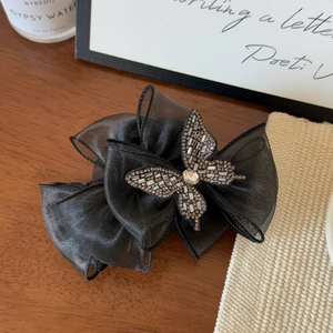 Détail d'une pince à cheveux à nœud en organza noir avec strass sur bois sombre
