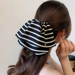Elegant black and white striped satin bow hair tie with a gold logo charm on a ponytail