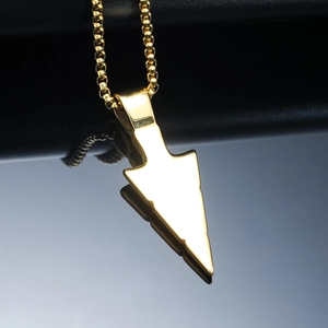 Close-up of golden stainless steel arrow pendant with smooth mirror finish on black texture