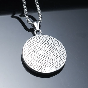 Macro shot of round stainless steel pendant with textured industrial finish on box chain