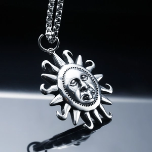 Polished stainless steel sun god face pendant with metal chain on reflective surface