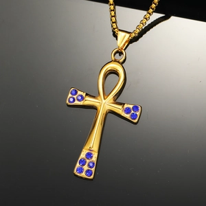 Macro shot of gold Ankh cross pendant featuring deep blue rhinestones on a mirror surface