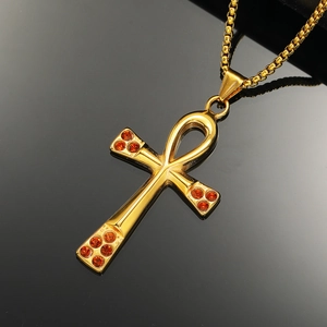 Macro shot of gold Ankh cross pendant with orange rhinestones on a black reflective base