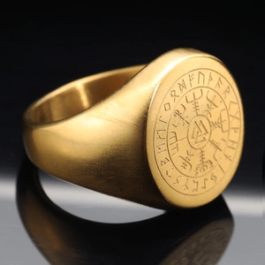 Anillo vikingo dorado con símbolo Valknut y brújula rúnica sobre superficie negra de espejo