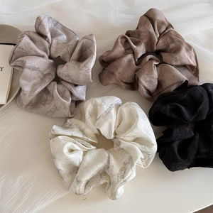 Close-up of four satin scrunchies featuring marble ink textures and smooth silk-like finish