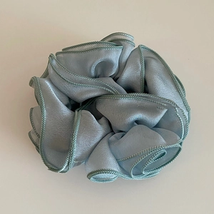 Dettaglio dello scrunchie a fiore in organza azzurra con bordatura verde finemente cucita