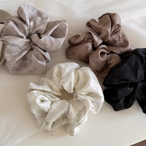 Close-up of four satin scrunchies with ink texture and marble patterns in neutral colors