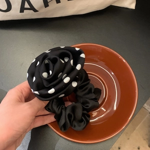 Close-up of a black polka dot camellia scrunchie with a French rose silk texture