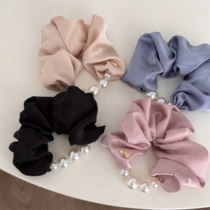 Détail de chouchous en satin de soie avec chaîne de perles et breloque logo dorée
