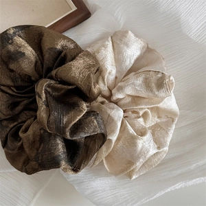 Close-up of silk-like oversized scrunchies in olive brown and champagne with glossy textures