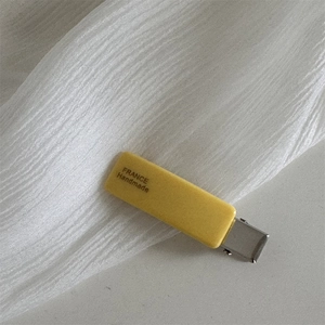 Detail view of yellow matte acetate hair clip with silver metal duckbill base and lettering