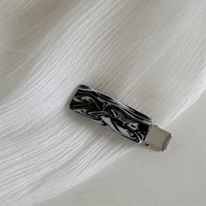 Close-up of rectangular black and white marble acetate hair clip with handmade script