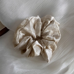 Detail of champagne satin scrunchie showing pleated silk texture and elegant metallic luster