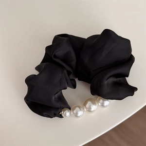 Détail d'un chouchou en satin noir avec d'élégantes perles blanches et une texture soyeuse