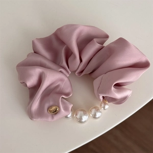 Vue détaillée du chouchou en satin rose poudré avec perles et étiquette dorée de luxe