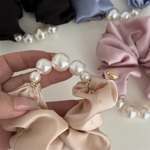 Gros plan du chouchou en satin champagne avec grandes perles et étiquette dorée