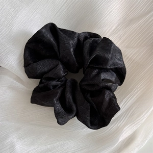 Close-up detail of black textured scrunchie with elegant pleated fabric and subtle sheen