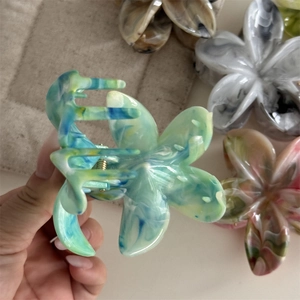 Detailaufnahme einer blau marmorierten Blumen-Haarklammer mit bunten Varianten im Hintergrund
