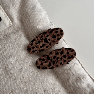 Close-up of two vintage leopard print hair clips on a white canvas bag strap