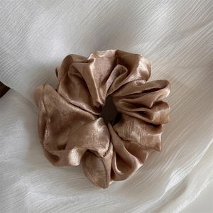 Close-up of champagne silk scrunchie with pleated texture on white fabric background