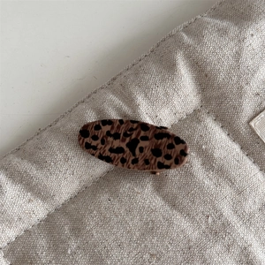 Detail shot of vintage leopard print oval hair clip on textured beige linen background