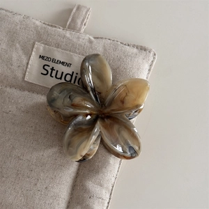 Detail einer marmorierten Haarklammer in Blumenform auf einem minimalistischen Leinenbeutel