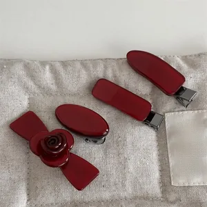 Close-up of four dark red acetate hair clips with metal alligator grip on canvas bag