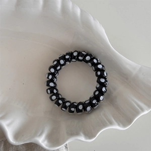 Polka dot spiral hair tie displayed in a white shell-shaped ceramic dish on linen fabric