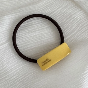Detail of yellow acetate charm on black elastic hair tie with France Handmade text