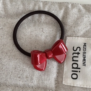 Close-up of elegant red acetate bow hair tie with glossy finish on textured linen