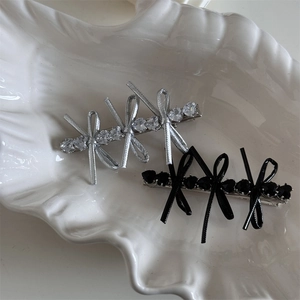 Detail of silver and black bow hair clips with heart stones on white shell plate