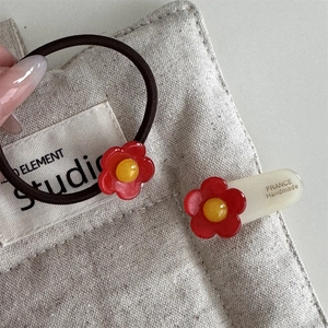 Detailansicht handgefertigter roter Blumenhaarklammern und Stirnband auf grauem Leinen